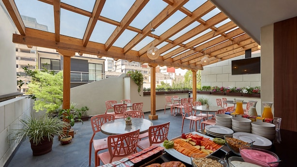 An outdoor patio with wooden beams, red chairs, a dining table with plates and food, and potted plants. - Senia Reforma (Mexico City)