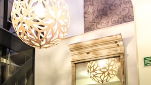 A lobby with two armchairs, a glass coffee table, a decorative hanging light fixture, and a large mirror reflecting the room. - Senia Reforma (Mexico City)