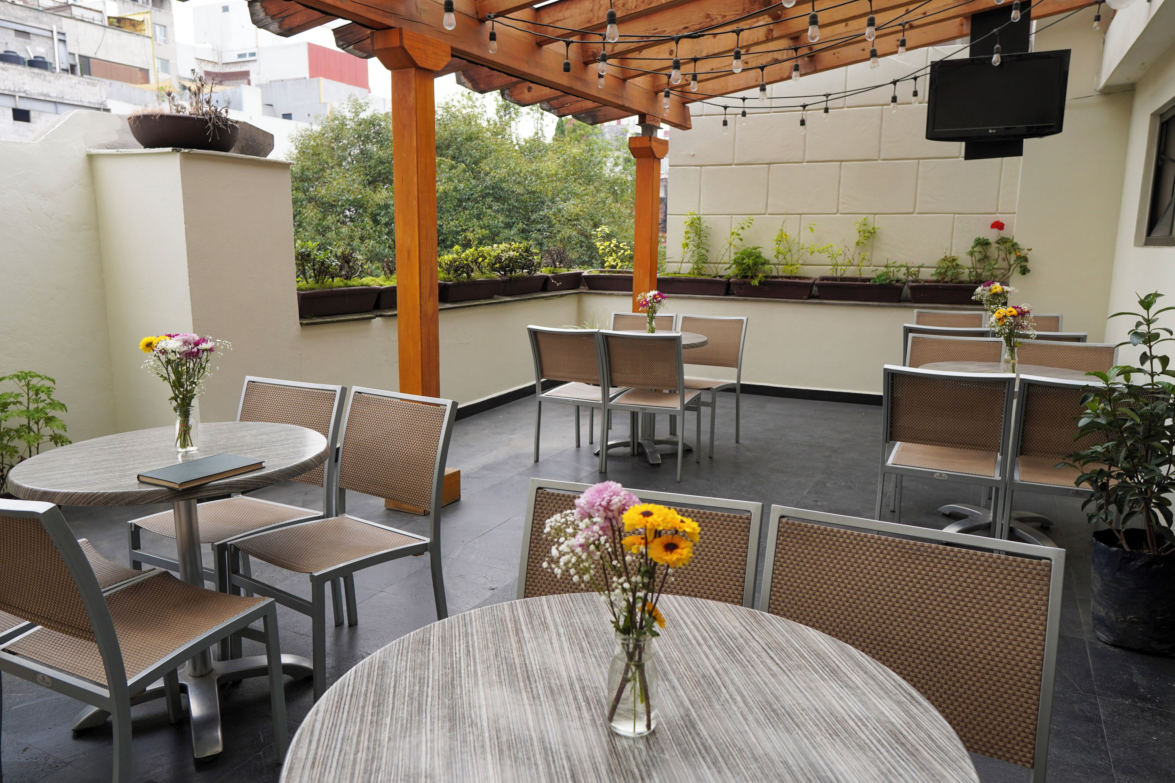 Un patio al aire libre con mesas y sillas redondas, algunas con jarrones de flores.