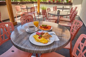Une table ronde avec une assiette de petit-déjeuner comprenant des toasts, des œufs et des fruits, ainsi qu'un verre de jus d'orange.