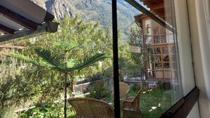 A balcony with wicker chairs, a glass door, and a view of a mountainous landscape. - Hotel Humantay Lodge Ollantaytambo (Ollantaytambo)