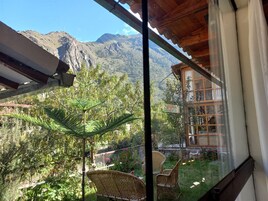 Un balcón con sillas de mimbre, una puerta de vidrio y vistas a un paisaje montañoso.