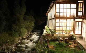 Un edificio a la orilla del río con una entrada bien iluminada y un área verde con sillas.