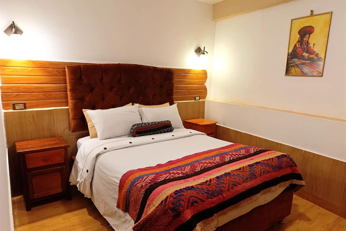 A neatly made bed with a patterned blanket, wooden headboard, bedside tables, and a wall-mounted light fixture.