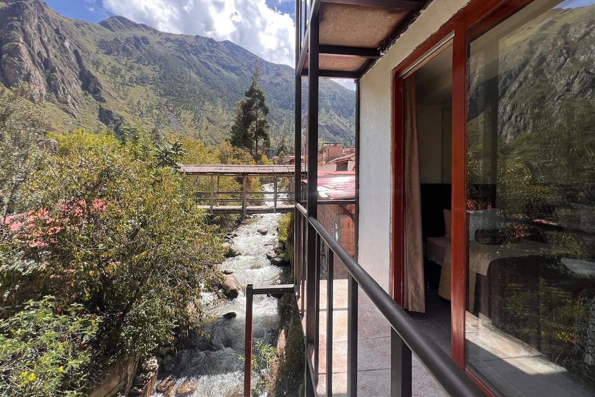 A balcony with a view of a mountain range, a small bridge, and a stream.