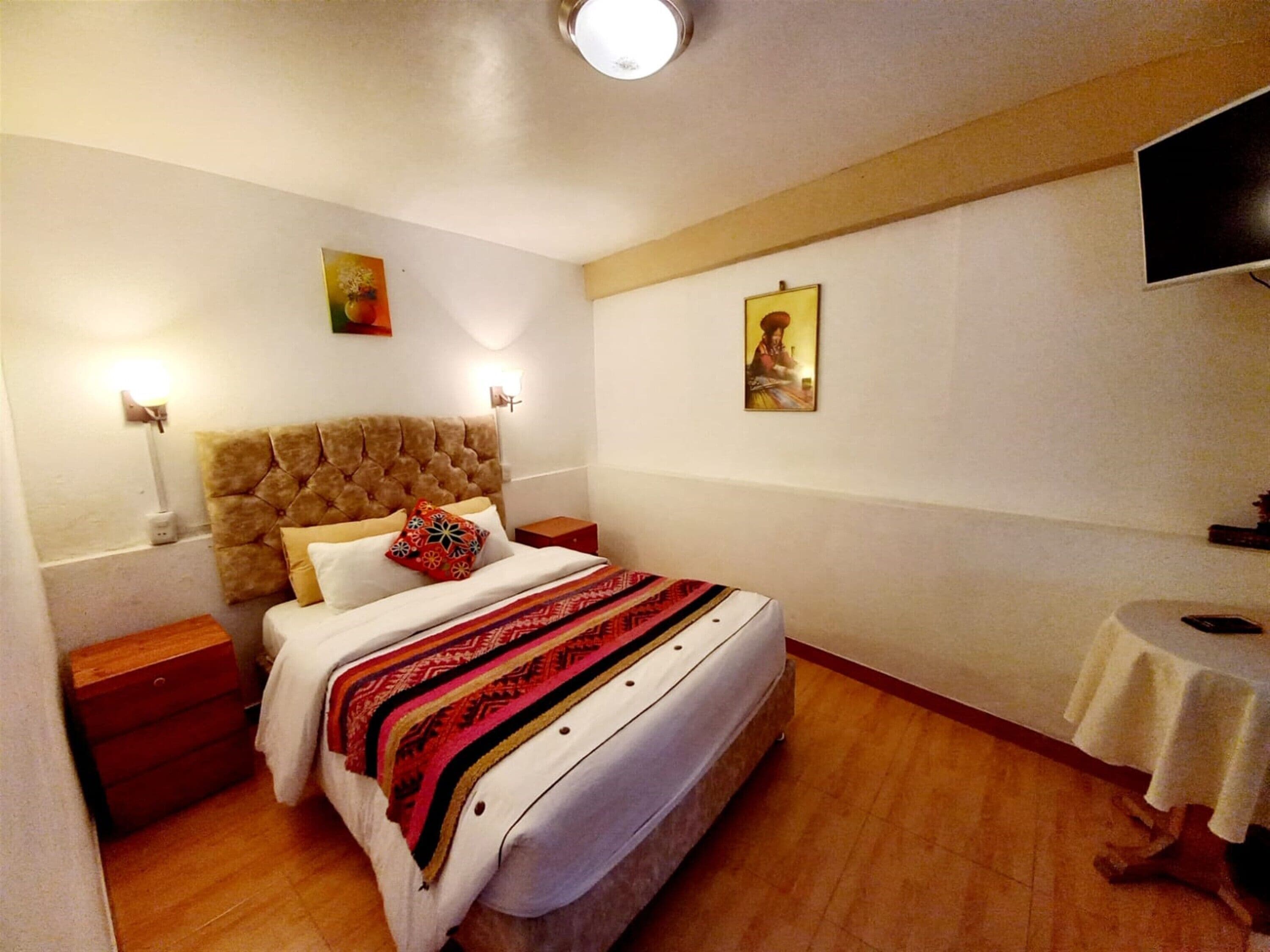 A hotel room with a large bed, a television on the wall, and a small table.