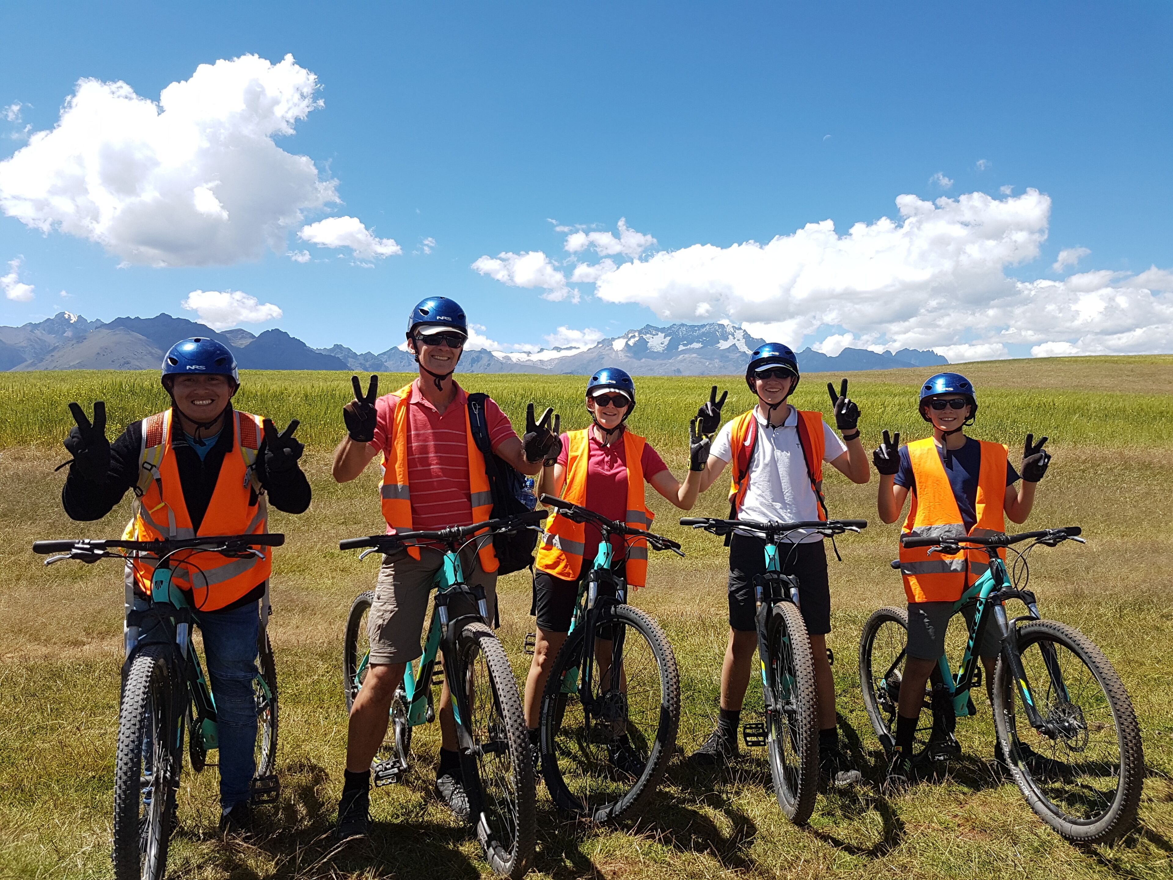 A group of five people on mountain bikes in a grassy field with a clear sky and mountains in the background.