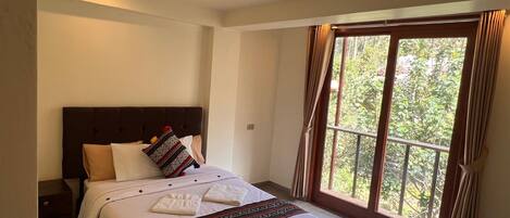 A neatly made bed with a headboard, a nightstand, and a window with curtains.
