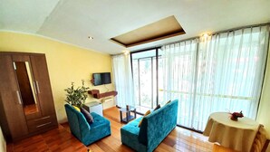A living room with a wooden floor, a blue sofa set, a TV mounted on the wall, and a large window with curtains. - Hotel Humantay Lodge Ollantaytambo (Ollantaytambo)
