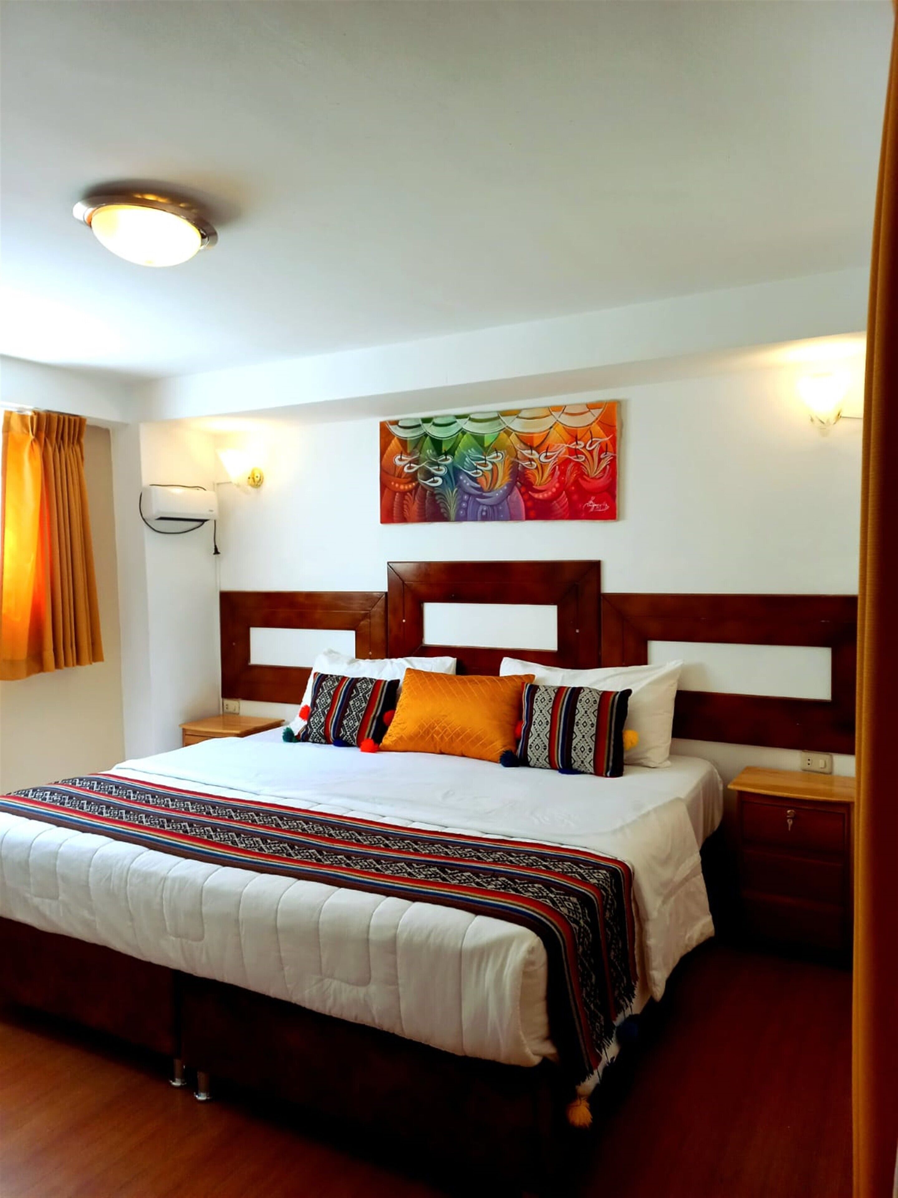 A hotel room with a large bed, wooden headboard, and a colorful abstract painting above it.
