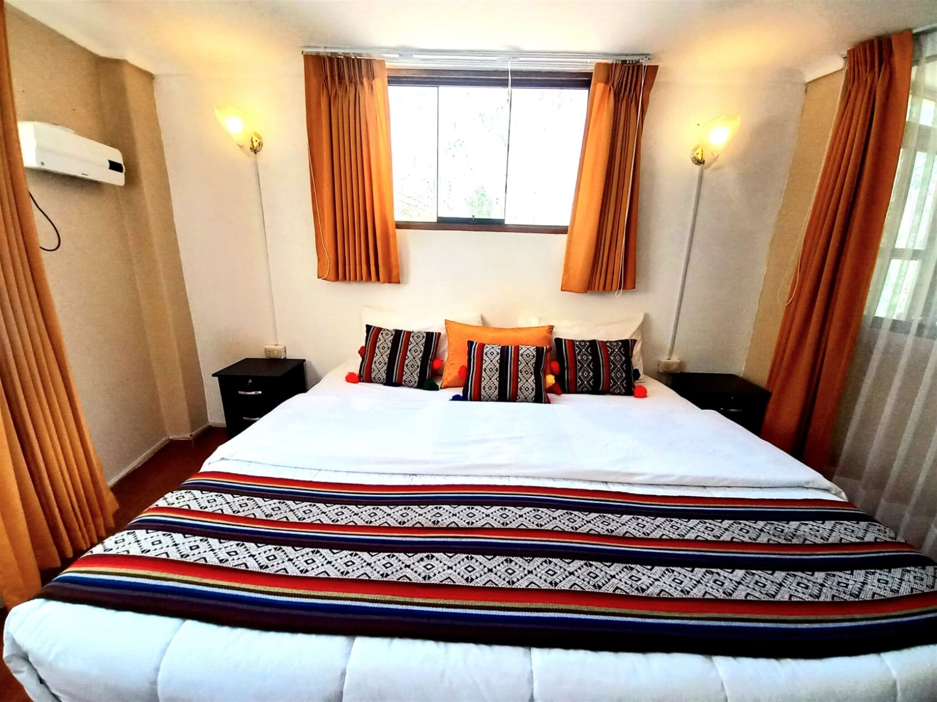 A hotel room with a large bed, two bedside tables, a window with curtains, and wall-mounted lights.