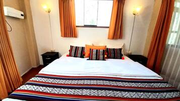 A hotel room with a large bed, two bedside tables, a window with curtains, and wall-mounted lights.