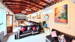A spacious living area with a high wooden ceiling, a black sofa with red cushions, a dining area with a long table, and a large painting on the wall. - Hotel Humantay Lodge Ollantaytambo (Ollantaytambo)
