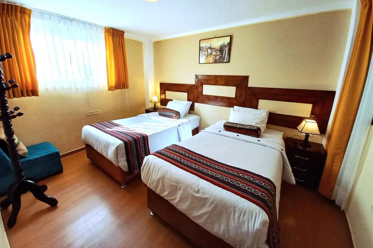 A hotel room with two beds, wooden headboards, a painting on the wall, and a desk with a lamp.