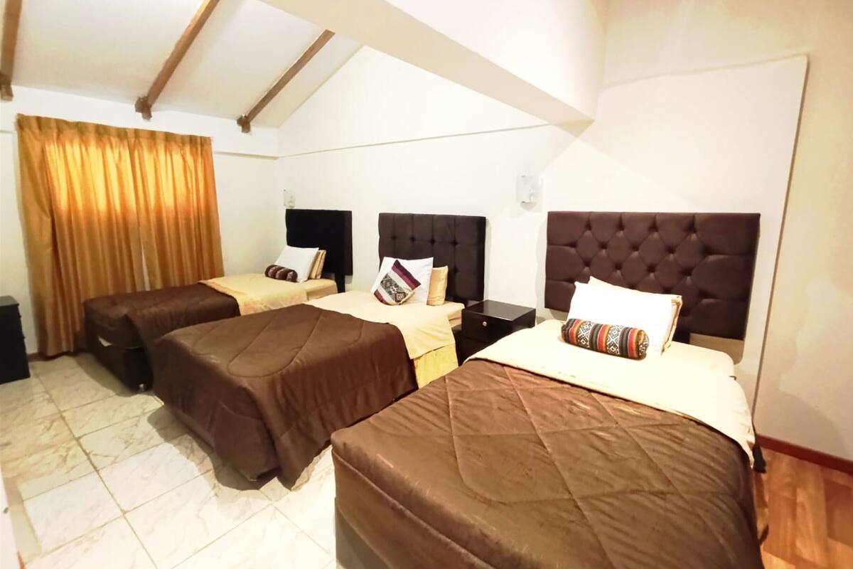 A hotel room with two single beds, a large bed, and a ceiling with exposed beams.