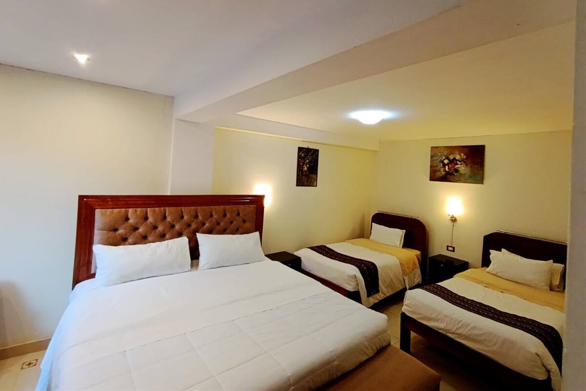 A hotel room with a large bed, two smaller beds, and a nightstand with a lamp.