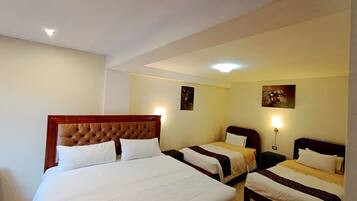 A hotel room with a large bed, two smaller beds, and a nightstand with a lamp.