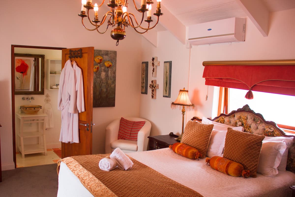 A bedroom with a large bed, a sitting area with a chair, a vanity with a mirror, and a chandelier.
