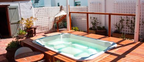 A wooden deck with a hot tub, outdoor seating, and potted plants.