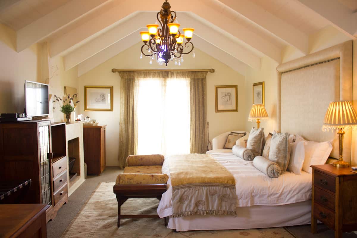 A bedroom with a large bed, a wooden dresser, a television, and a chandelier.