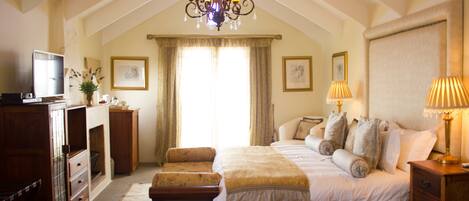 A bedroom with a large bed, a wooden dresser, a television, and a chandelier.