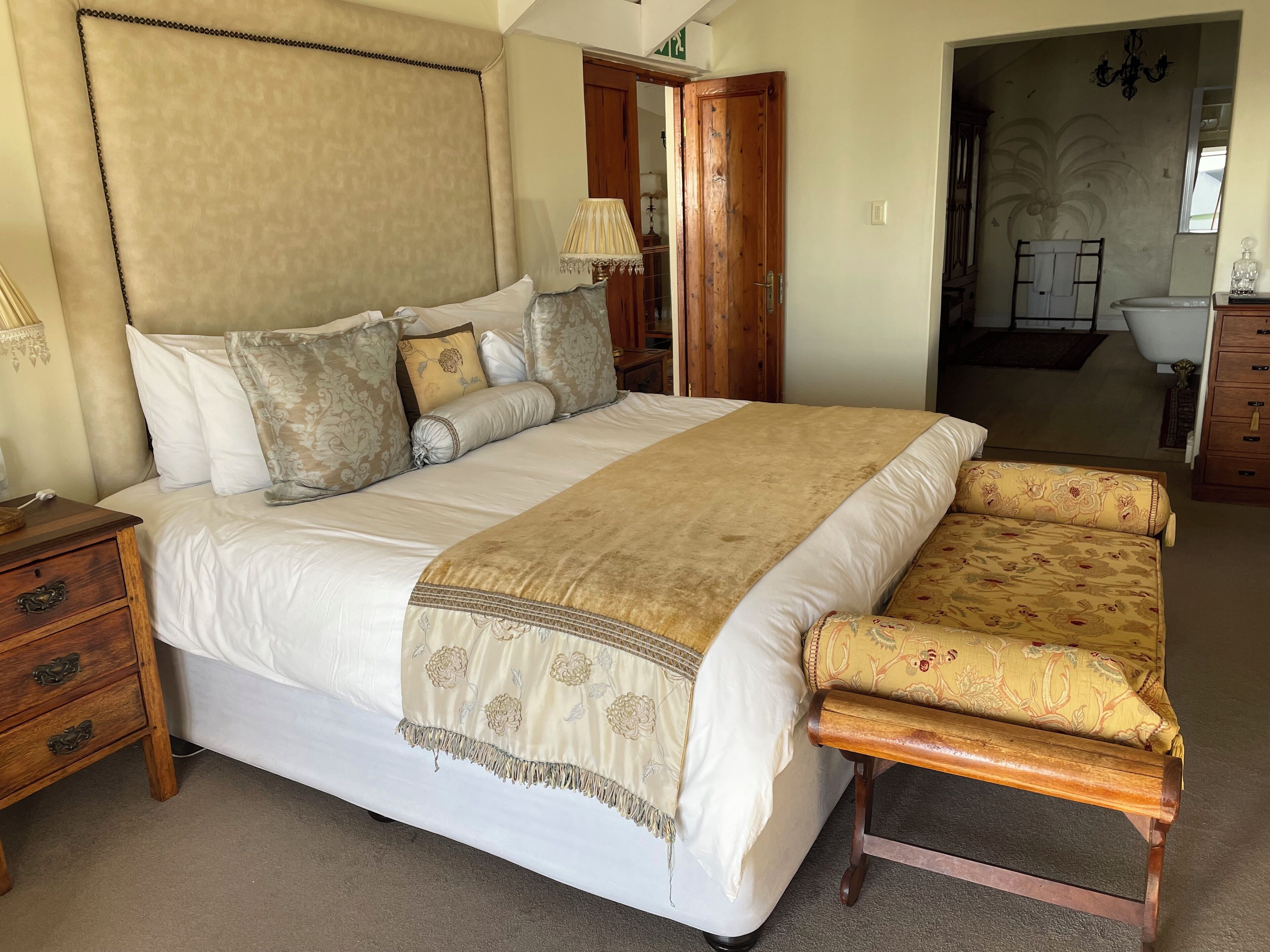 A large bed with a beige headboard, multiple pillows, and a wooden bench.
