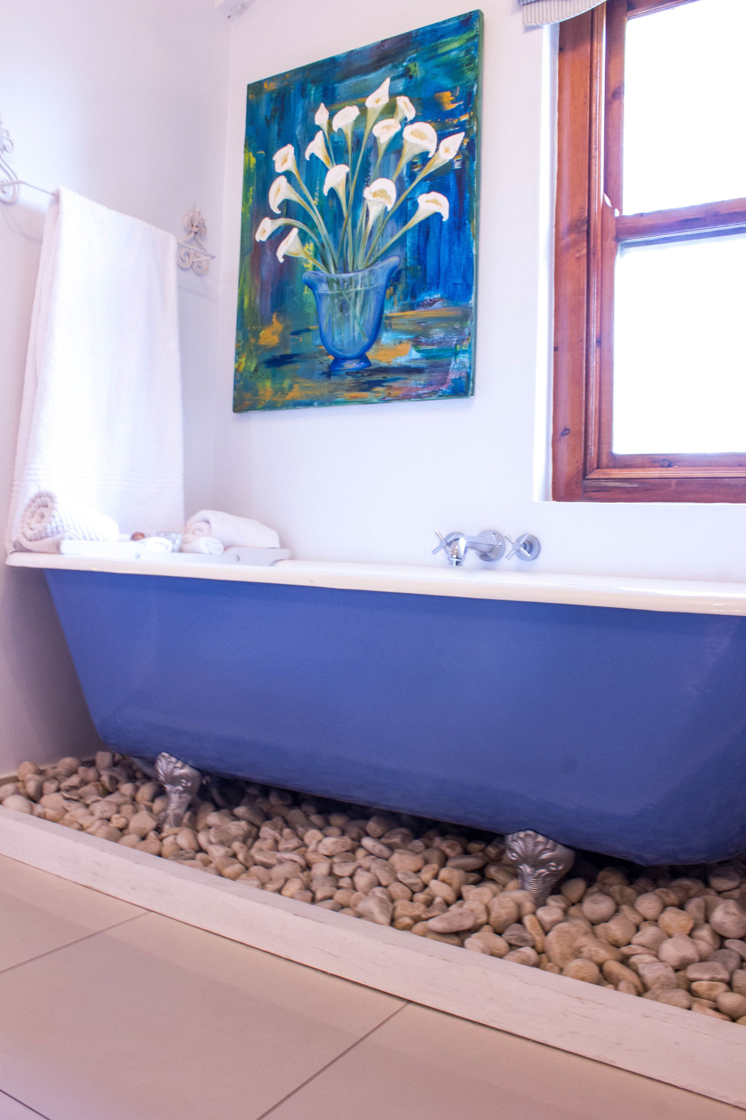 Un baño con una bañera azul, un cuadro de flores en la pared y una ventana.