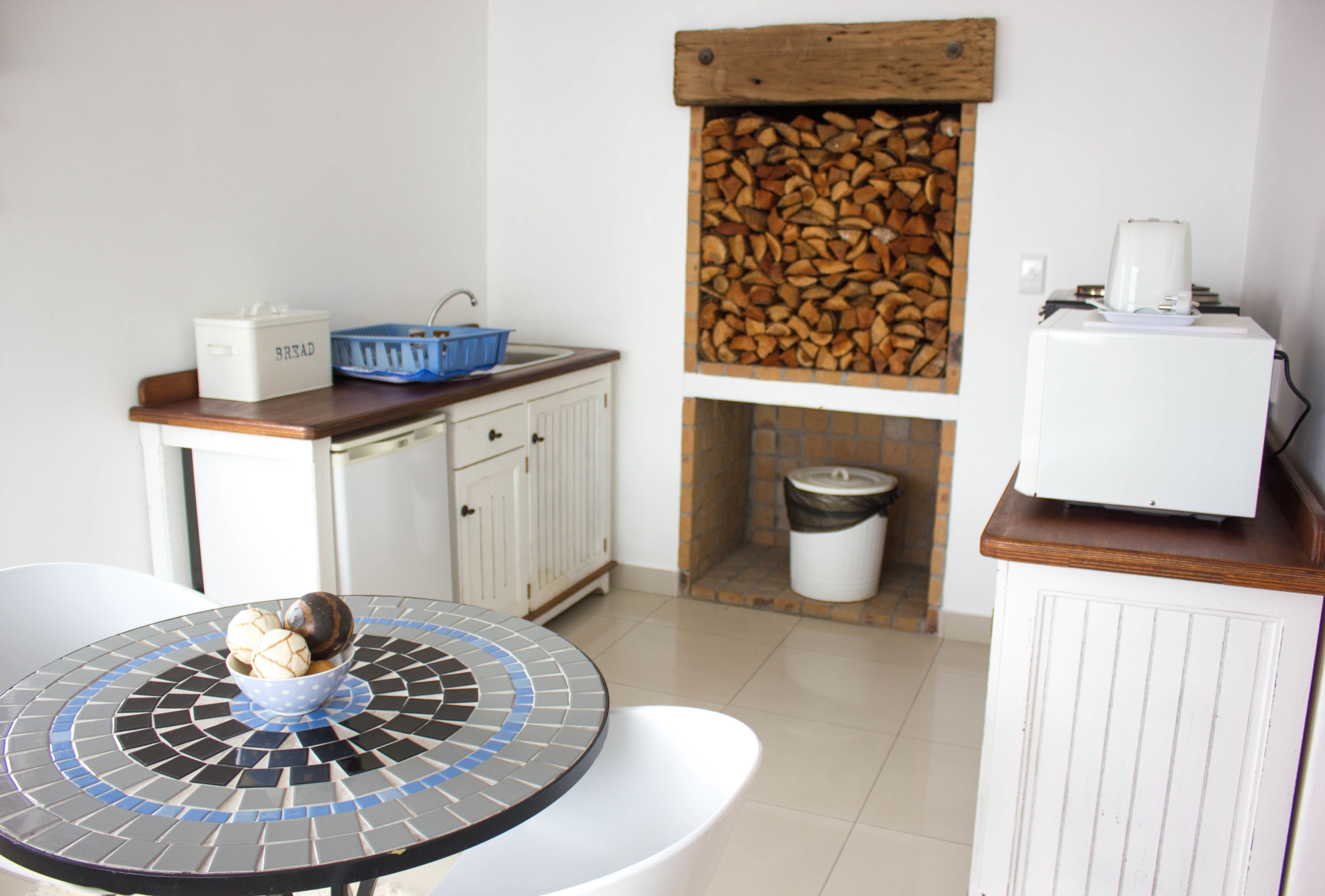 A compact kitchen with a round table, a blue basket, a bread box, a wooden log storage, and a white refrigerator.