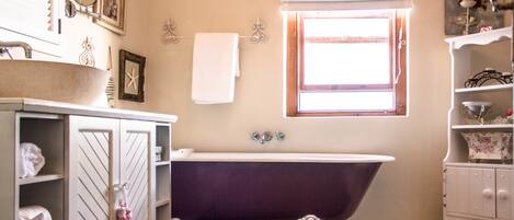 A bathroom with a freestanding bathtub, a vanity with shelves, and a window with curtains.