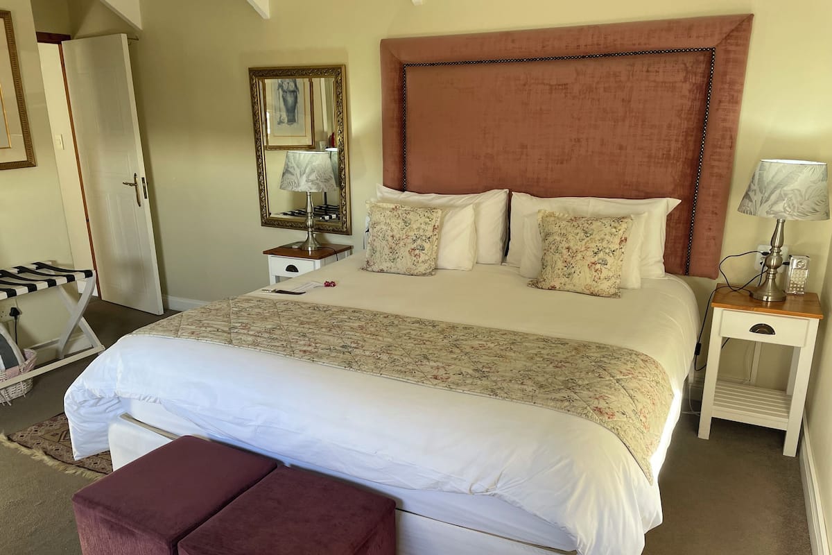 A neatly arranged bedroom with a large bed, a bedside table with a lamp, a mirror, and a wardrobe.