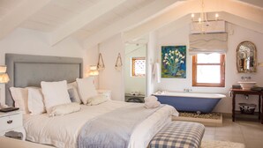 A bedroom with a large bed, a bathtub, and a vanity with a mirror. - Paternoster Manor (Paternoster)