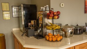 A kitchen counter with a refrigerator, a microwave, a coffee maker, a fruit basket with apples and oranges, and a slow cooker. - Richland Inn Lawrenceburg (Lawrenceburg)