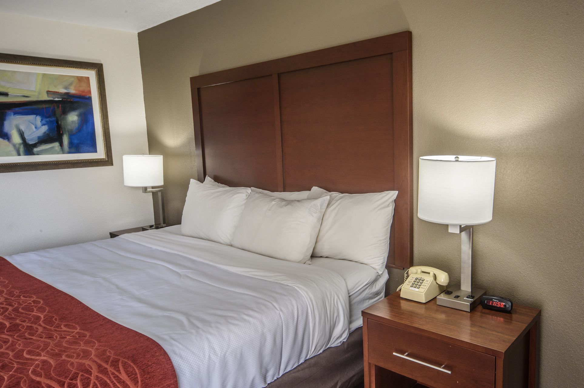 A hotel room with a large bed, two bedside lamps, a bedside telephone, and a painting on the wall.