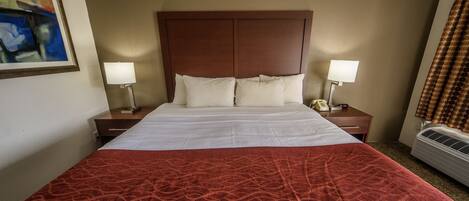 A hotel room with a large bed, two bedside tables with lamps, a wall-mounted air conditioner, and a painting on the wall.