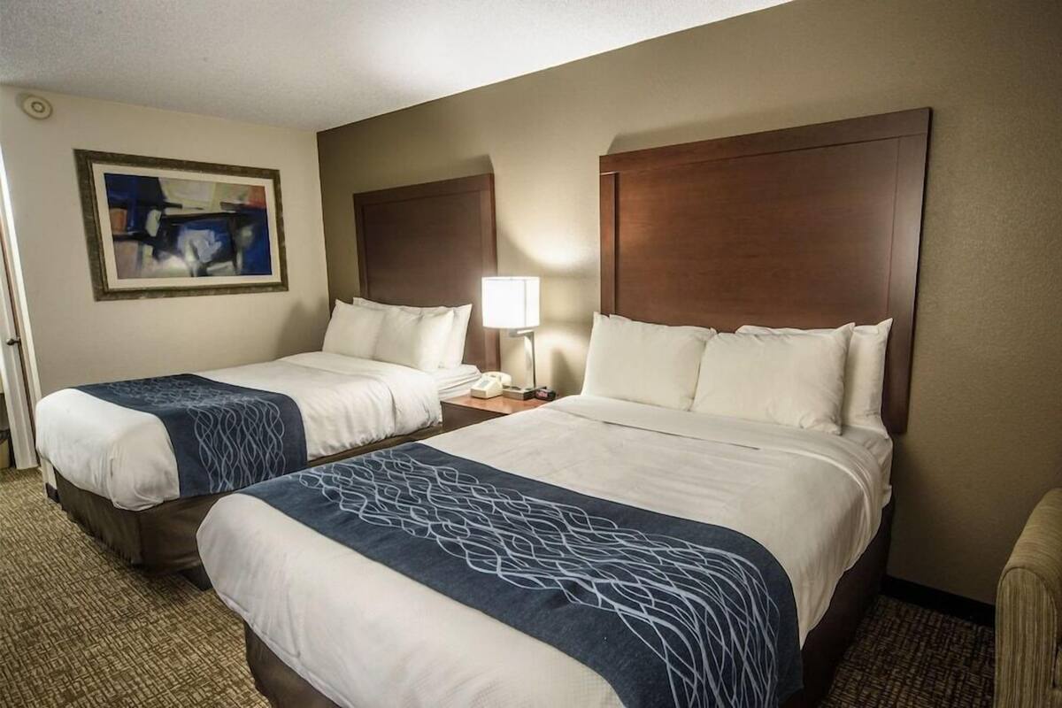 A hotel room with two beds, a nightstand, a lamp, and a painting on the wall.