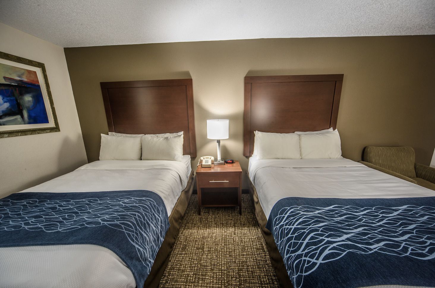 A hotel room with two beds, a nightstand with a lamp, and a painting on the wall.