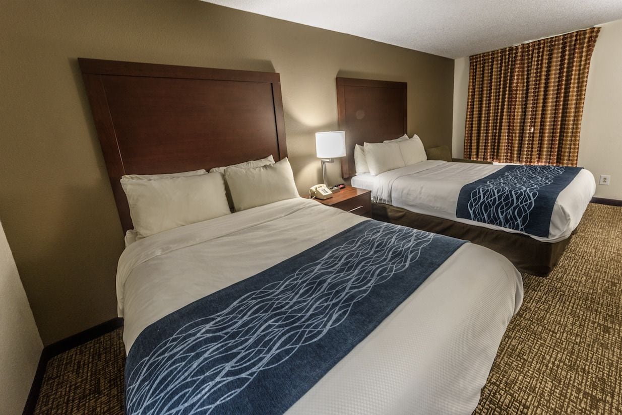 A hotel room with two beds, a nightstand with a phone, and a patterned throw blanket.