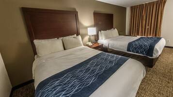 A hotel room with two beds, a nightstand with a phone, and a patterned throw blanket.
