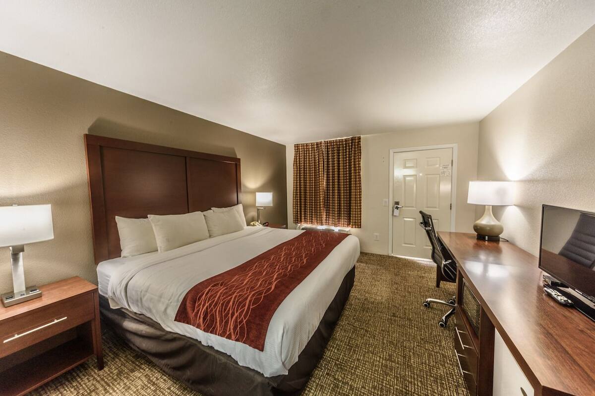 A hotel room with a large bed, a desk with a chair, a TV, and a door.