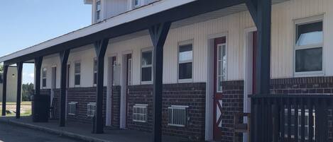 A row of single-story buildings with a covered walkway, brick walls, and a mix of red and white doors.