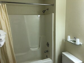 A bathroom with a glass shower enclosure, a toilet, and a shelf with cups. - Quik Stop and Motel (Wausaukee)