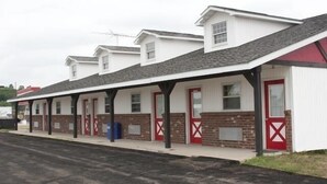 A row of single-story buildings with brick lower floors and white upper floors, featuring red doors and a covered walkway. - Quik Stop and Motel (Wausaukee)