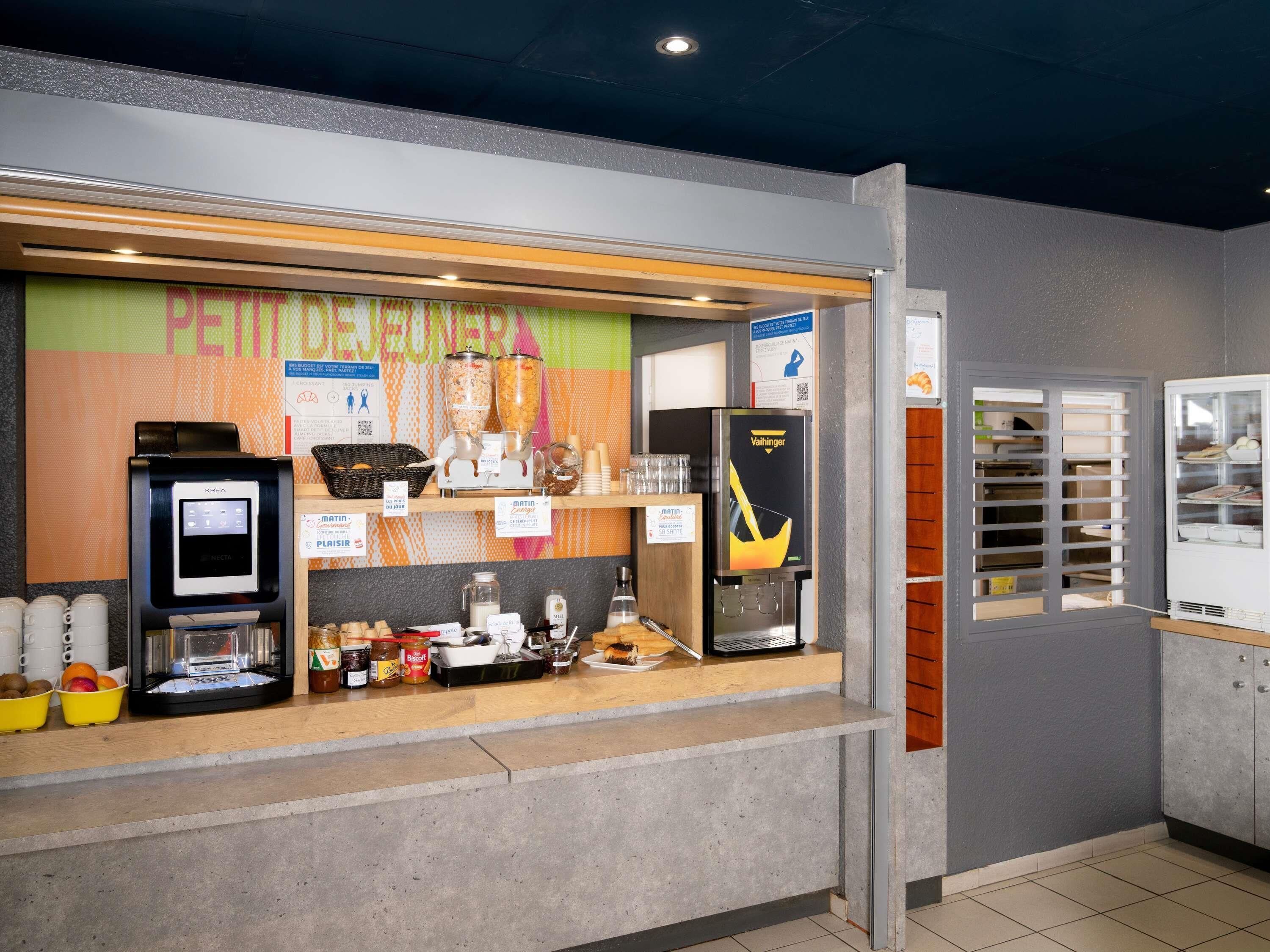 Una estación de desayuno autoservicio con una máquina de café KREA, un dispensador de café Vaillant y diversas opciones de comida.