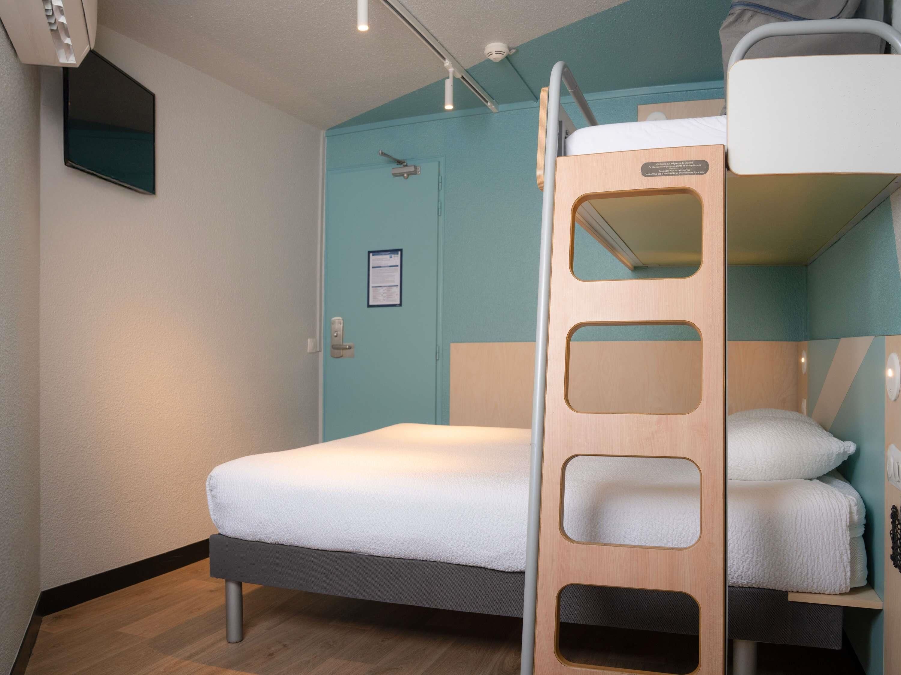 A bunk bed room with a wooden ladder, a door with a notice, and a small window.
