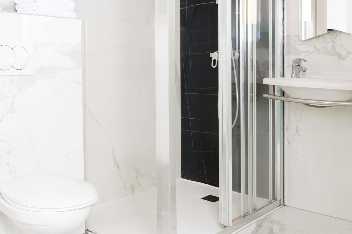 A modern bathroom with a glass-enclosed shower, a white toilet, and a marble-tiled floor.