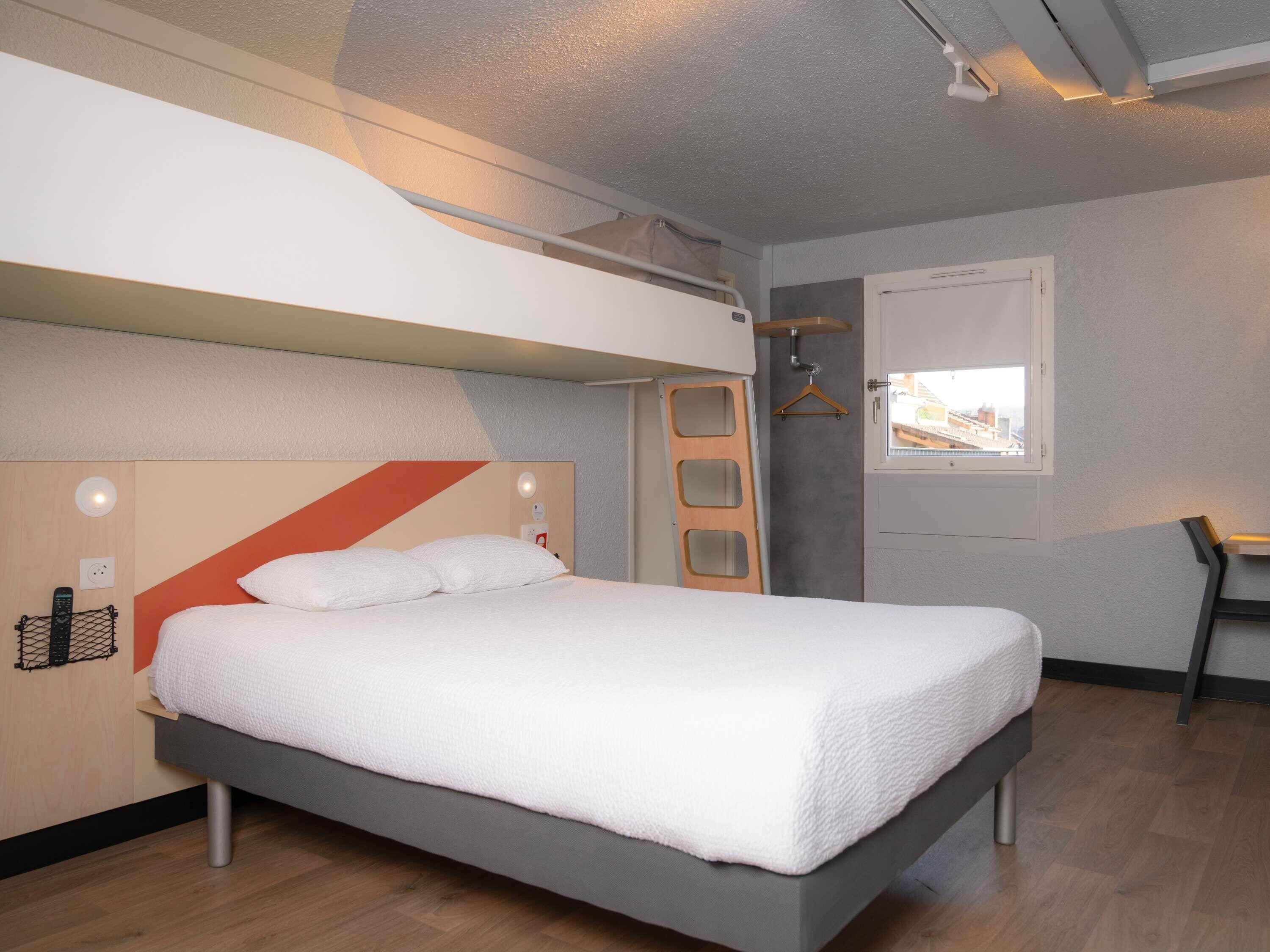 A modern hotel room with a bed, a desk, and a window.
