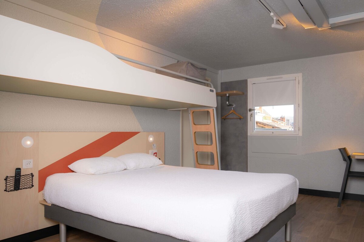 A modern hotel room with a bed, a desk, and a window.