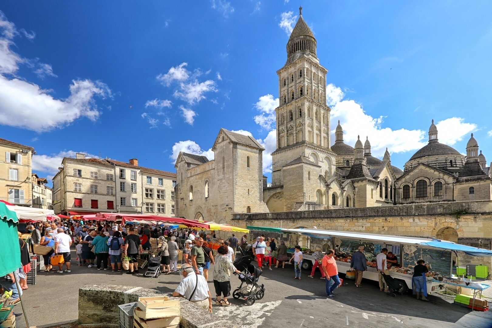 Un marché animé en plein air, avec des bâtiments historiques et une tour imposante en arrière-plan.