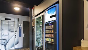 Un distributeur automatique proposant diverses collations, une porte sur laquelle est apposée une plaque indiquant « CHAMBERS », et un plancher en bois.