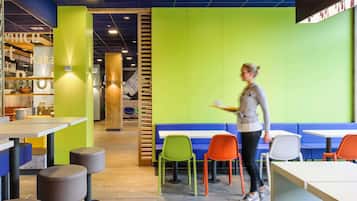 Una cafetería moderna con suelo de madera, paredes verdes y sillas coloridas.